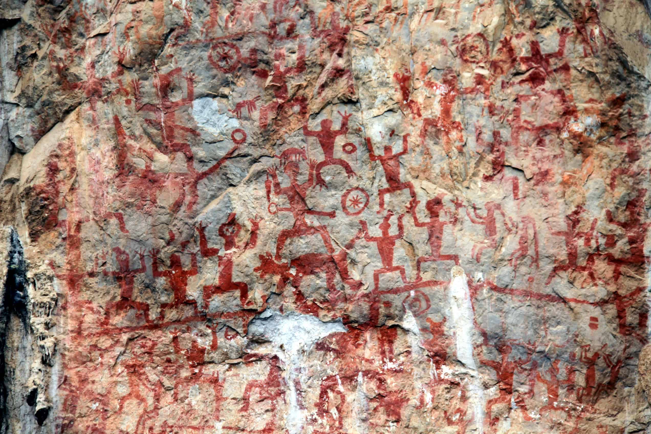 Red painted figures appear across the weathered limestone surface of the Zuojiang Huashan rock paintings in Guangxi, China.