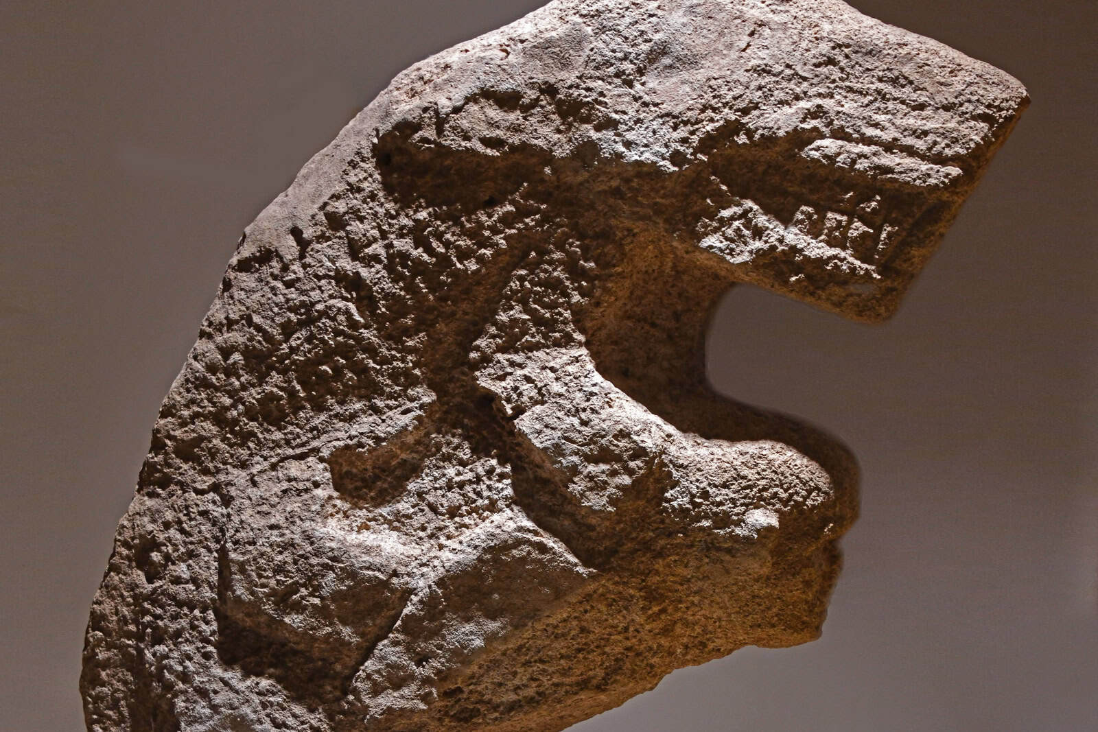 A museum display of the weathered limestone sculpture identified as a human carrying a leopard on its back.