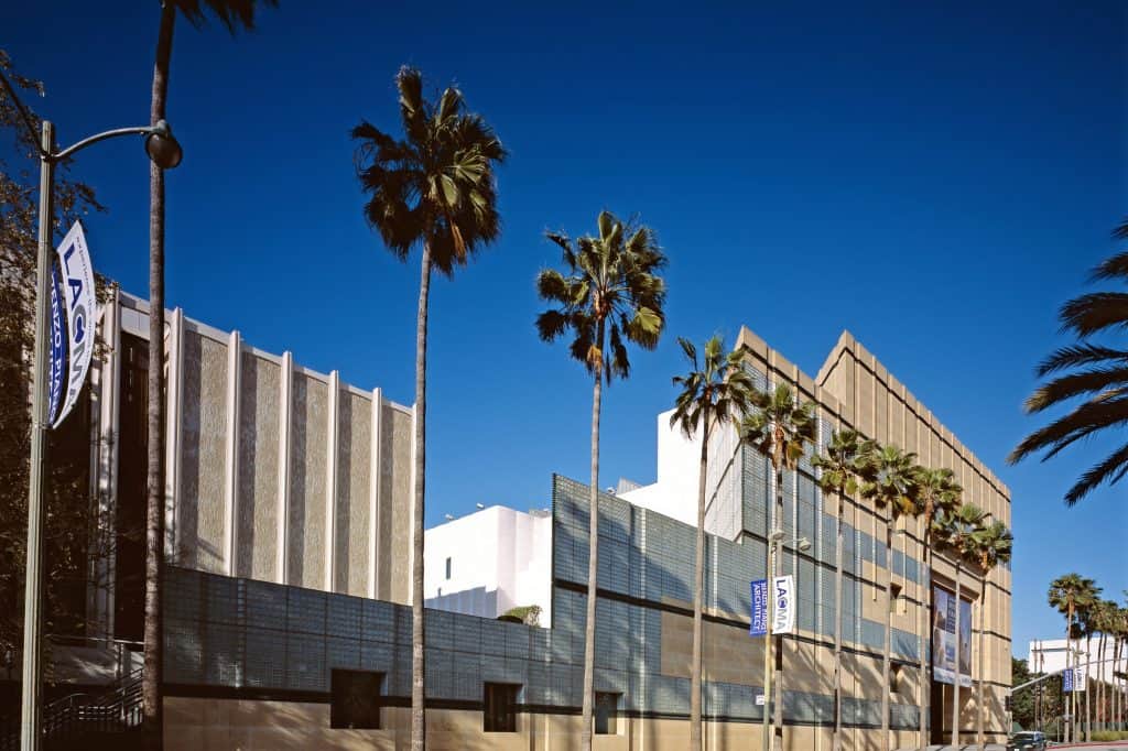 An oblique daylight view shows the Los Angeles County Museum of Art complex and palm trees along Wilshire Boulevard.