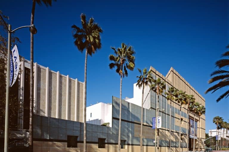 An oblique daylight view shows the Los Angeles County Museum of Art complex and palm trees along Wilshire Boulevard.