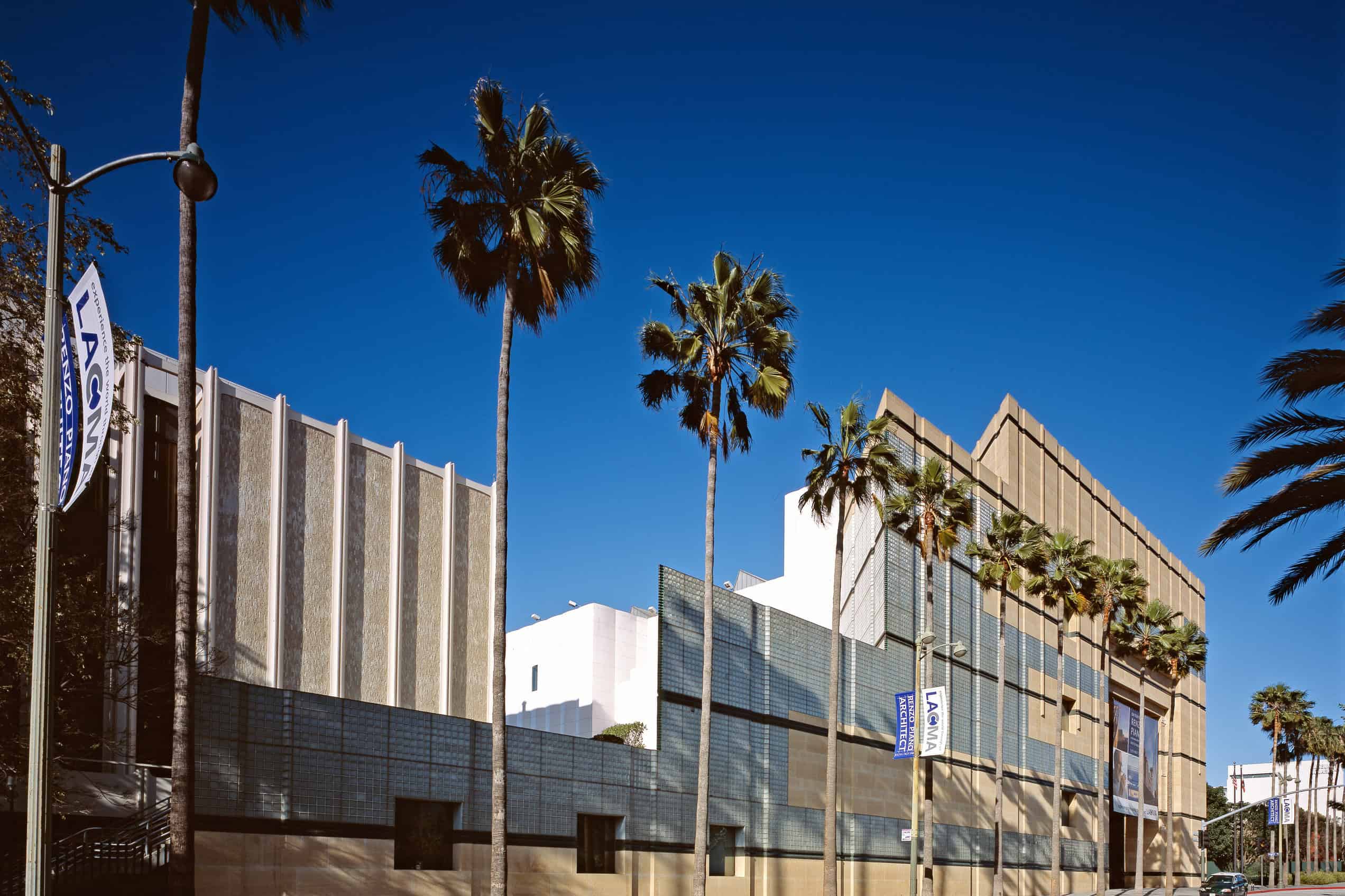 An oblique daylight view shows the Los Angeles County Museum of Art complex and palm trees along Wilshire Boulevard.