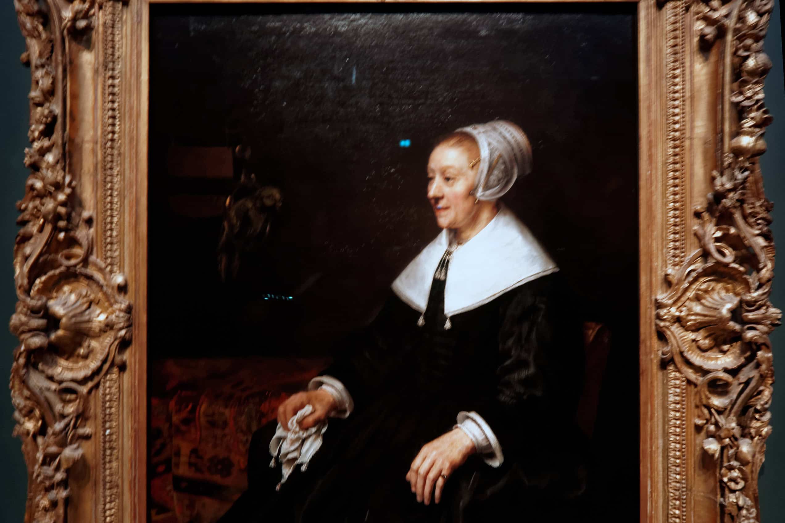 Catrina Hooghsaet sits in a black silk dress and white cap, holding a handkerchief beside a parakeet in Rembrandt’s 1657 portrait.