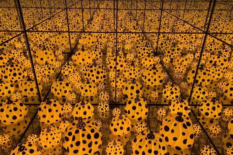 A yellow room covered in black dots surrounds a mirrored chamber filled with repeating pumpkin forms.