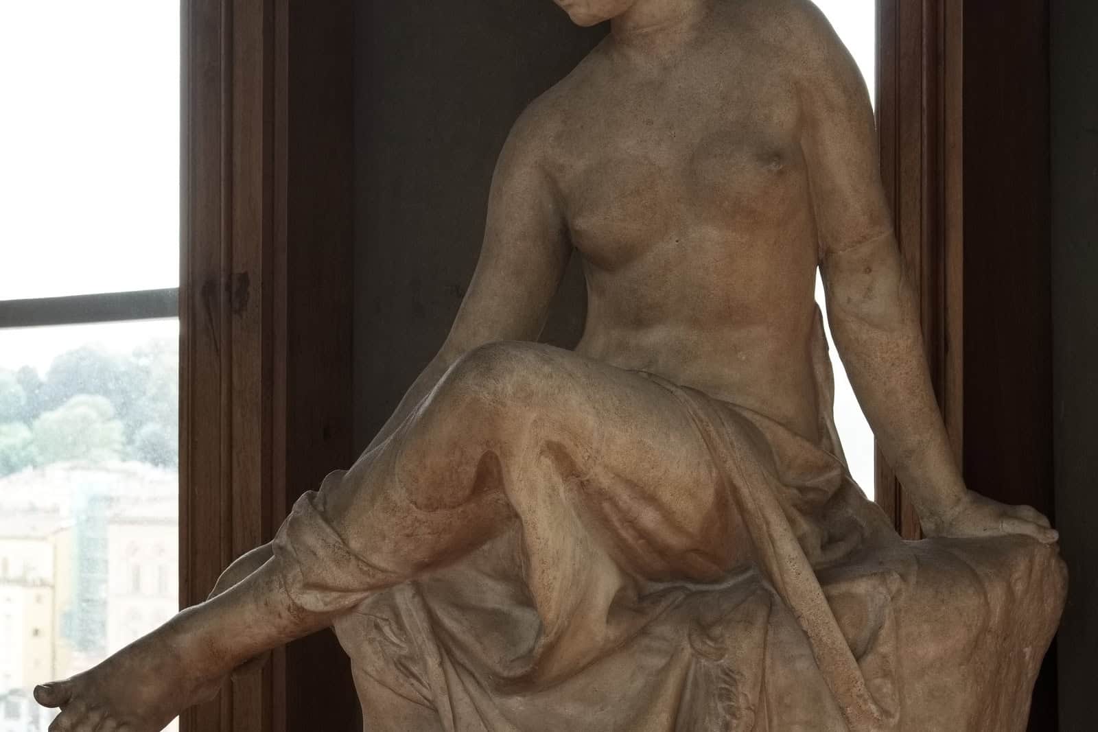 A restored Roman marble nymph sits on a rock with her draped legs crossed and one hand reaching toward her foot.