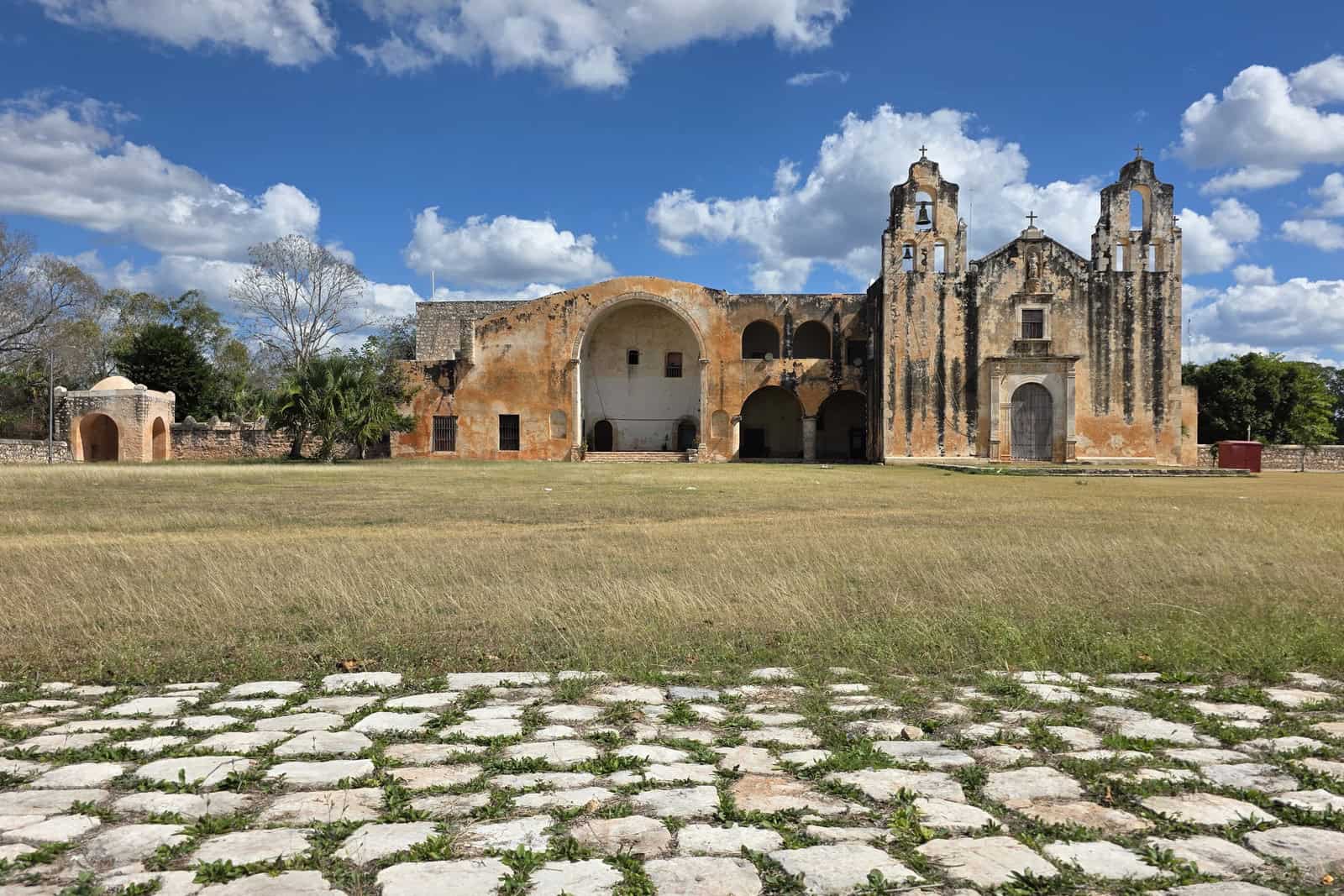 The pale stone façade and twin bell towers of the former Convent of Saint Michael the Archangel in Maní under a blue sky.