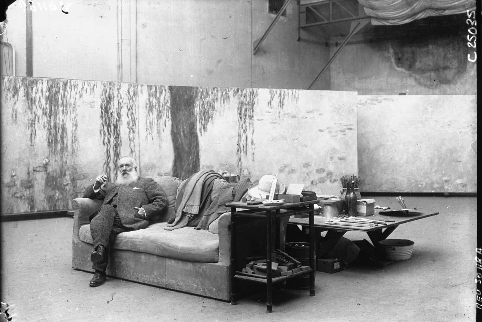 Claude Monet stands in his studio among monumental canvases in a 1926 press photograph.