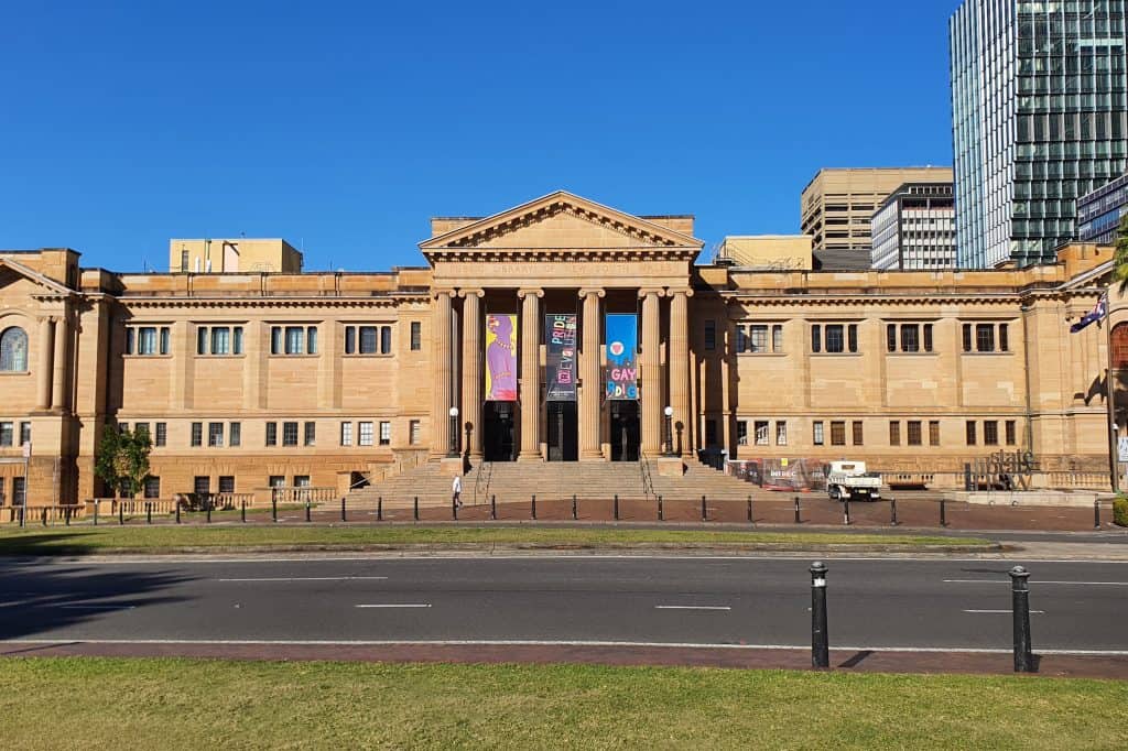The sandstone facade and columned entrance of the State Library of New South Wales stand beneath a blue Sydney sky.