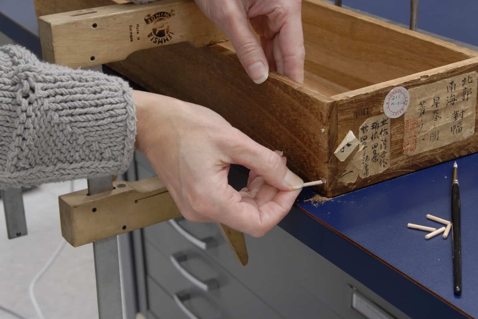 Museum conservation technician repairing a Japanese scroll box at a worktable