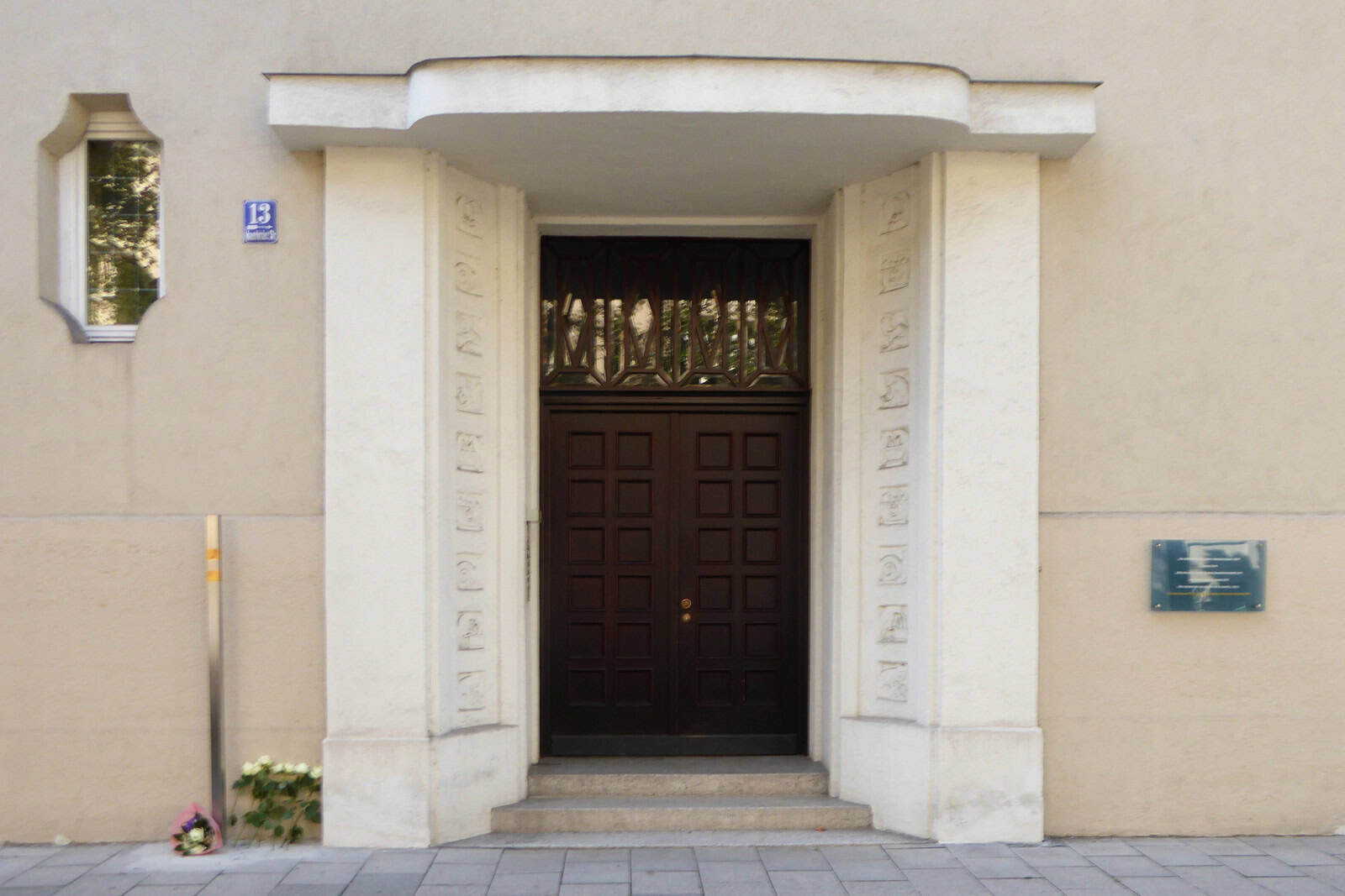 A gilded memorial stele stands beside the entrance of a residential building in Munich.