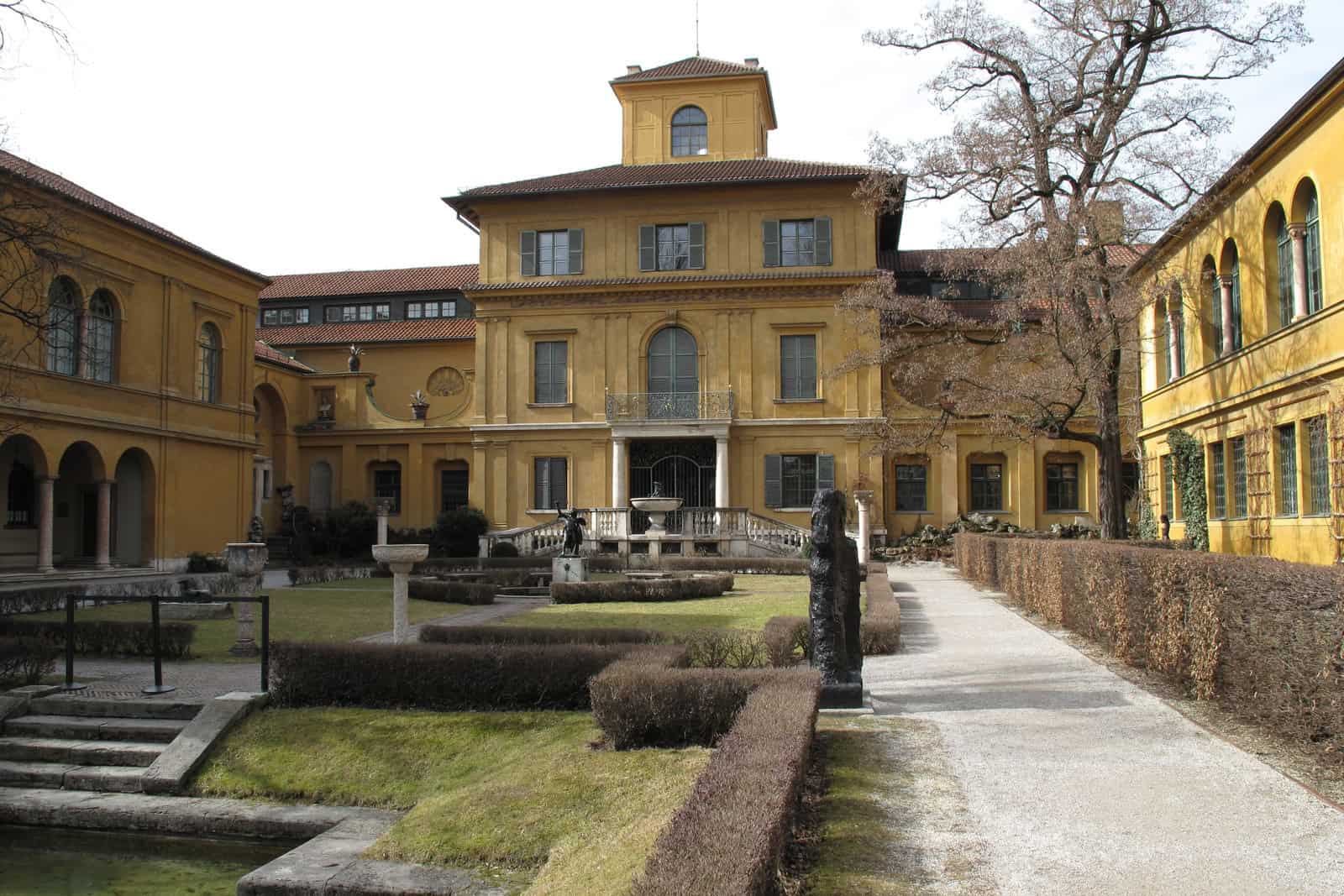 The historic yellow Lenbachhaus building stands behind a stone garden wall in Munich.