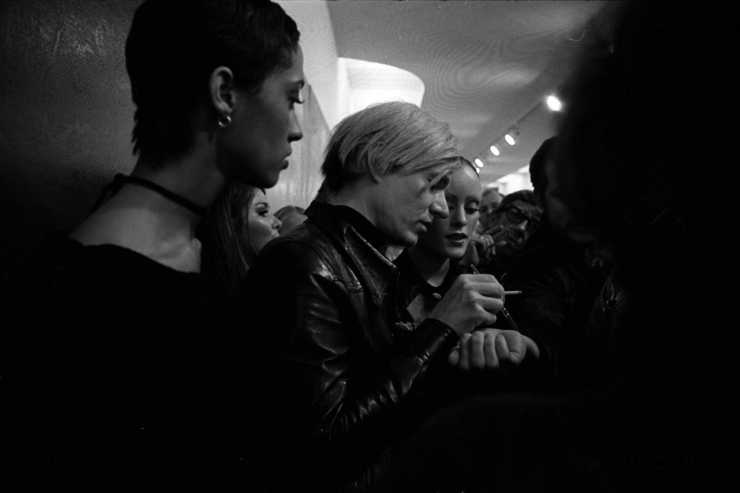 Andy Warhol leans over a table while signing autographs at the Pasadena Art Museum in 1970.