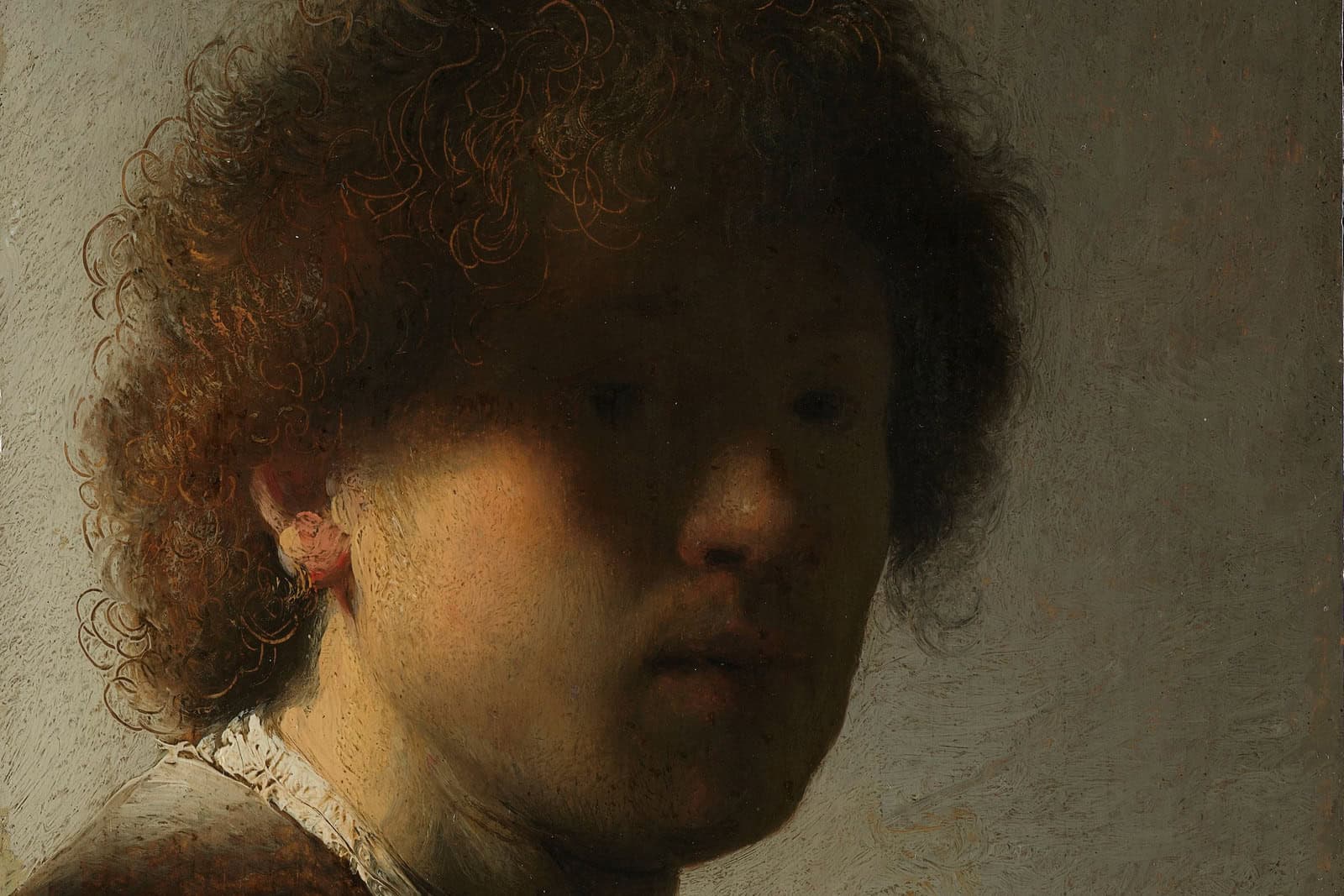 A young Rembrandt turns toward the viewer while most of his face remains in shadow beneath tousled curls.
