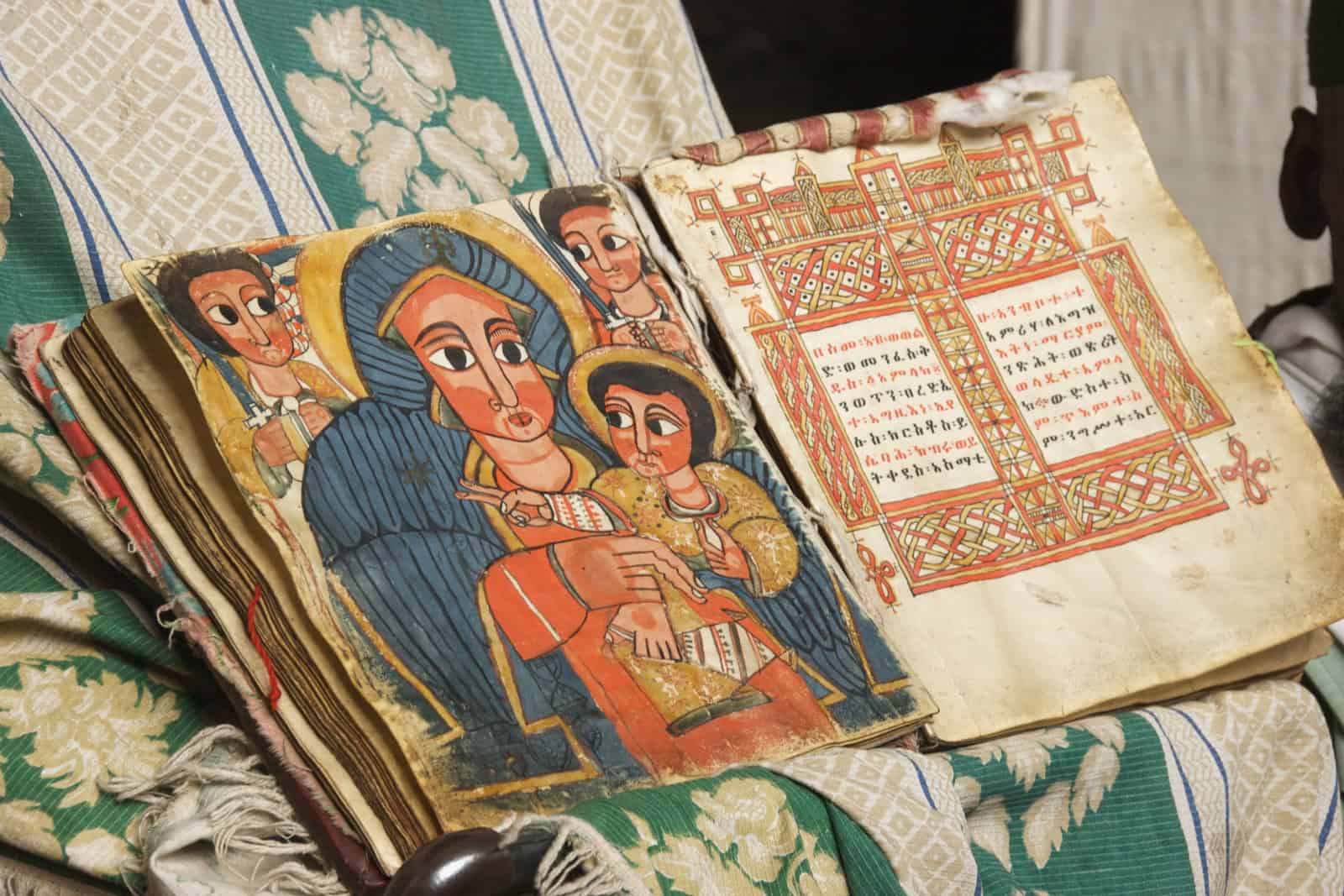 Open Ethiopian manuscript with an illuminated religious painting and lines of Ge'ez text.