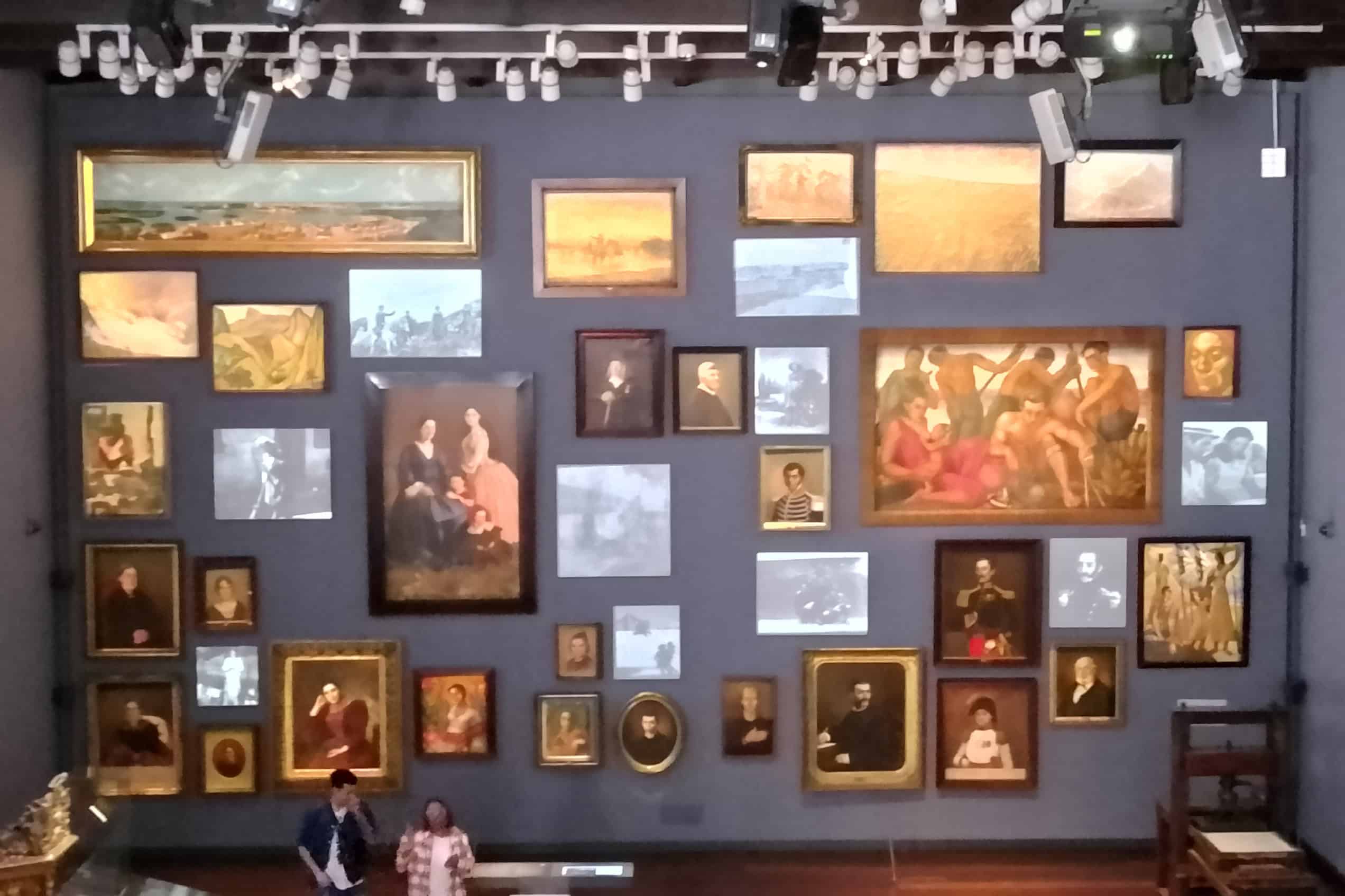 A wall of framed portraits, paintings and projected faces inside the Museo Nacional de Colombia’s Memoria y Nación gallery.
