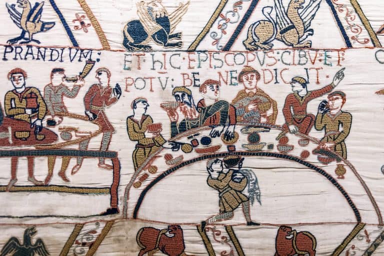 Bishop Odo raises one hand to bless a meal while Norman nobles sit around a curved table in the Bayeux Tapestry.