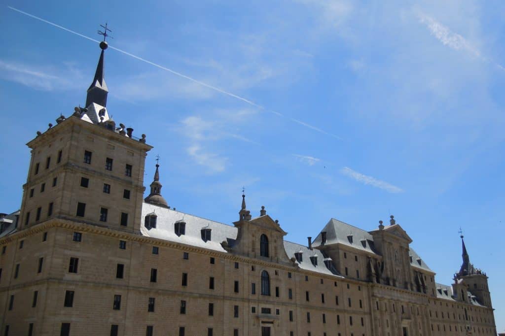The broad stone west façade of the Royal Monastery of San Lorenzo de El Escorial beneath a blue sky.