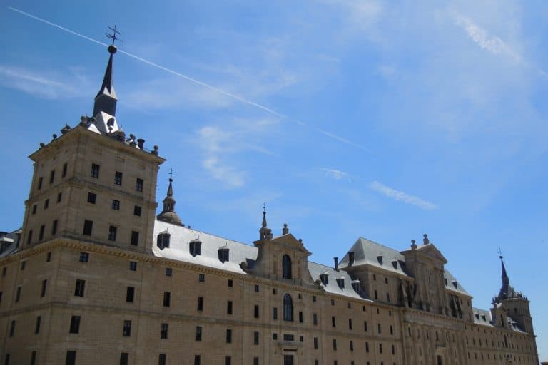 The broad stone west façade of the Royal Monastery of San Lorenzo de El Escorial beneath a blue sky.