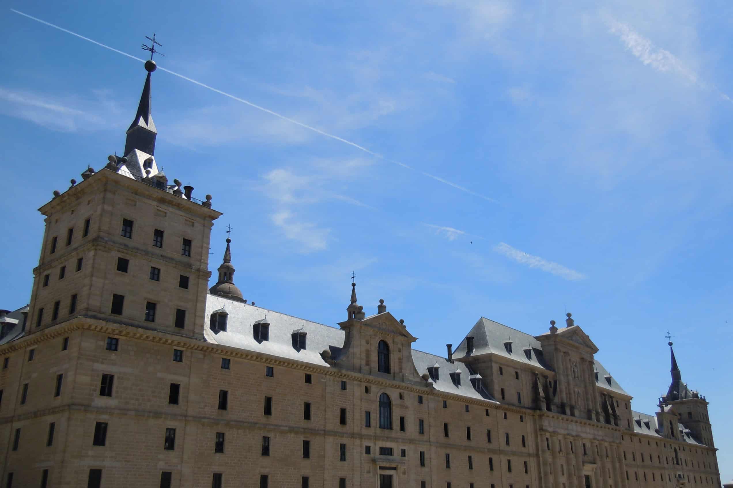 The broad stone west façade of the Royal Monastery of San Lorenzo de El Escorial beneath a blue sky.
