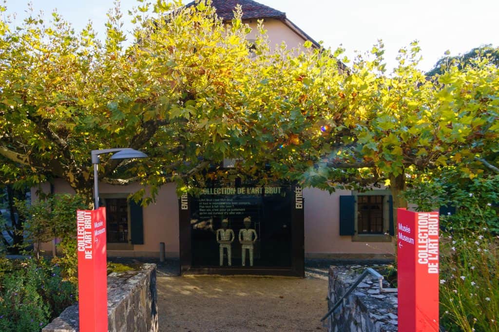 The pale stone exterior and tiled roof of the Collection de l’Art Brut in Lausanne are seen from its courtyard.