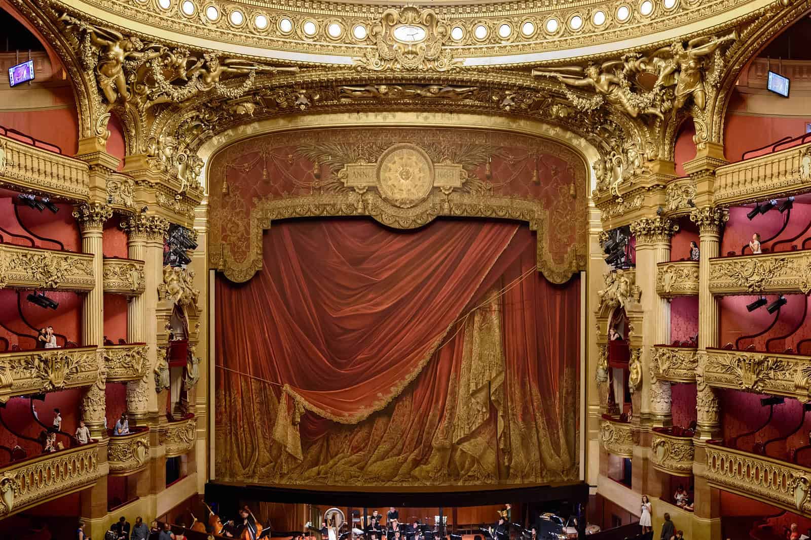 Wide panoramic view of the red-and-gold Palais Garnier auditorium and stage.