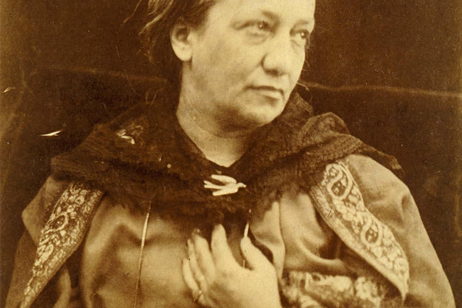 Julia Margaret Cameron sits in a patterned shawl and lace veil, with her hands in her lap and her gaze turned to the side.