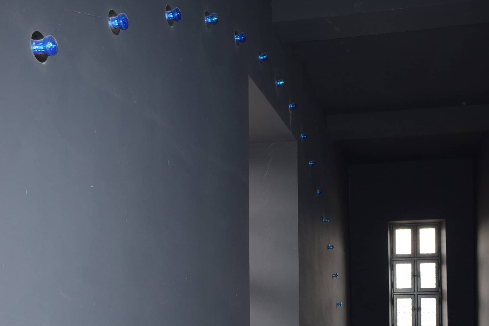 Blue illuminated installation extending vertically through the interior of the Musée Rimbaud.