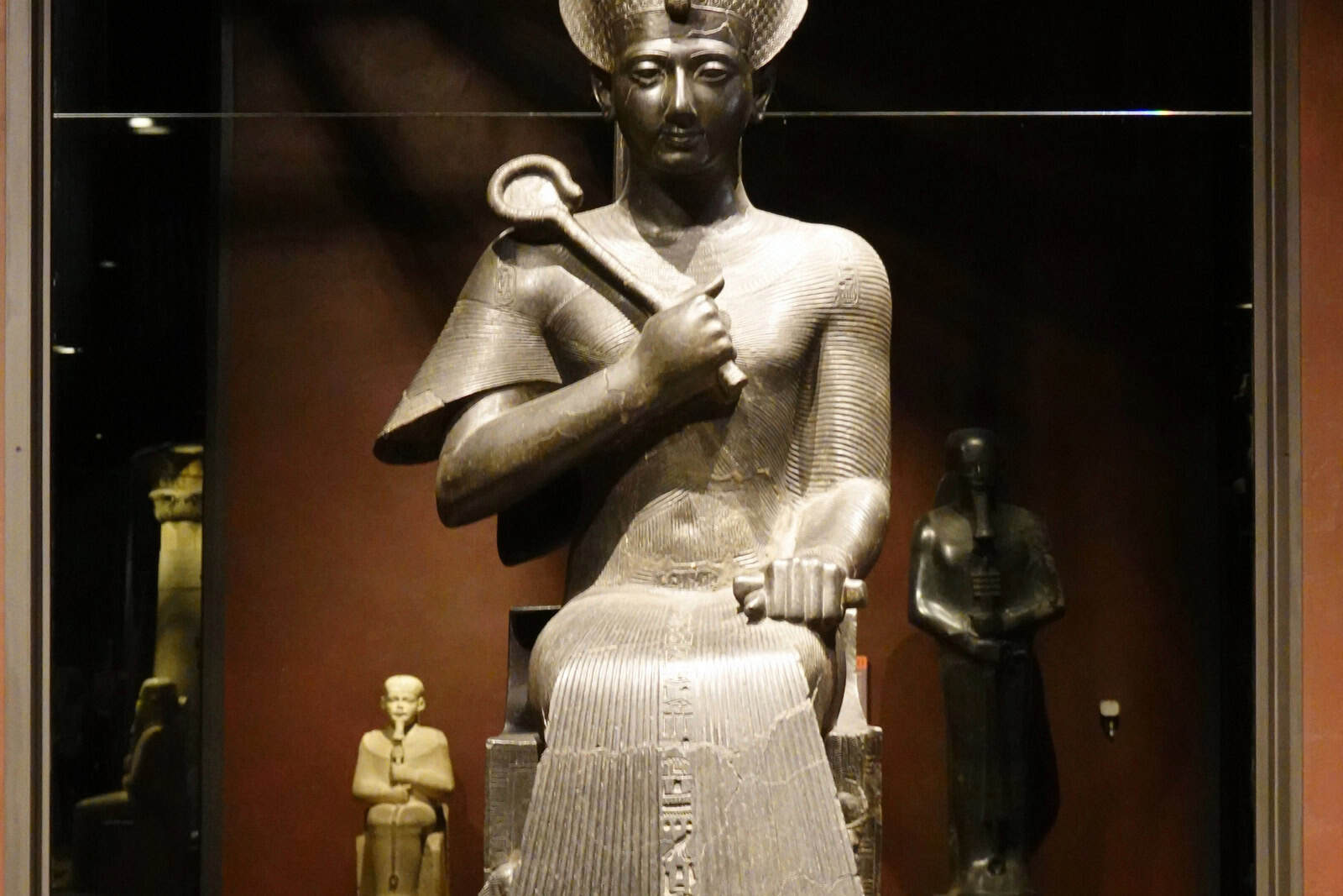 A granodiorite statue of Ramses II stands against a dark museum background.