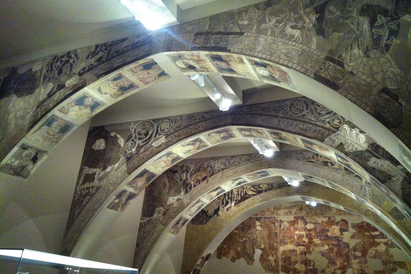 The fire-damaged chapter-house paintings from Santa María de Sijena displayed on arches at the MNAC.